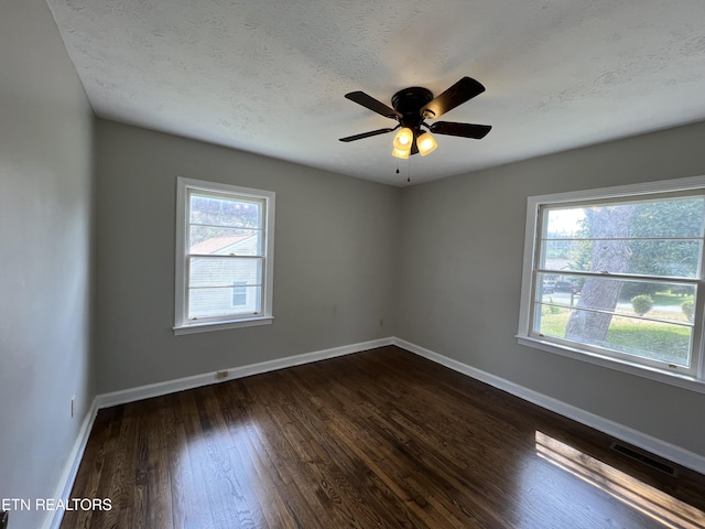 unfurnished room with a healthy amount of sunlight, dark wood-type flooring, baseboards, and visible vents