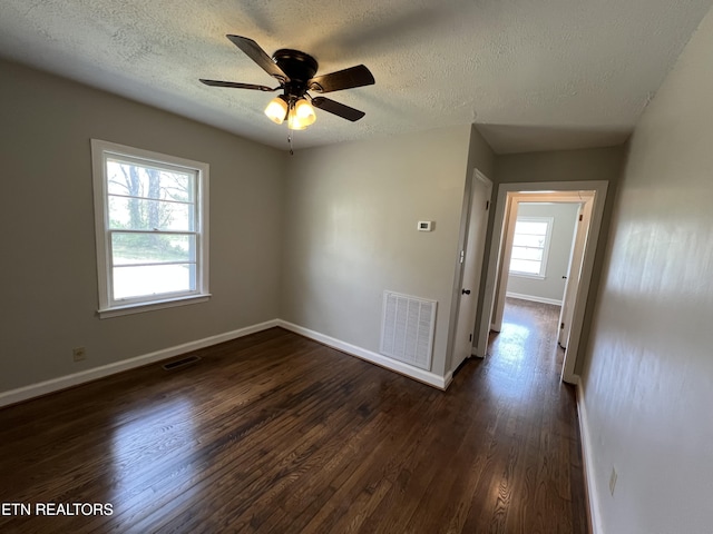 empty room featuring baseboards, visible vents, dark wood-type flooring, and a ceiling fan