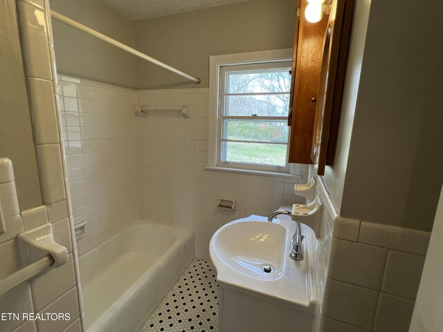bathroom with a sink, shower / bath combination, tile walls, and wainscoting