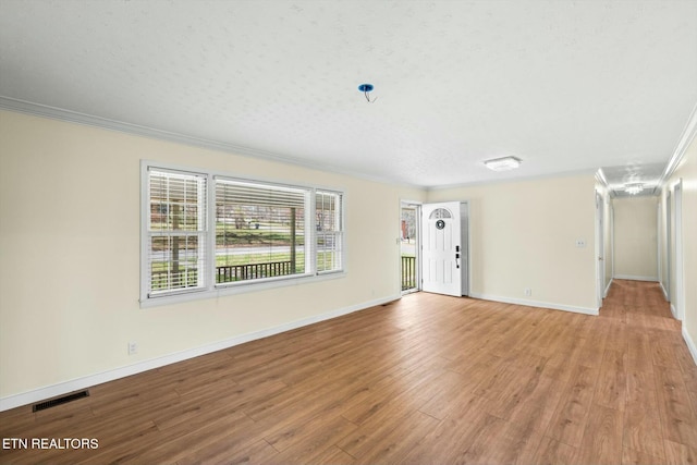 unfurnished living room featuring light wood-style flooring, ornamental molding, baseboards, and visible vents