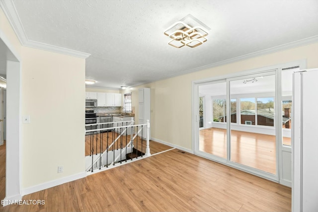 interior space featuring crown molding, a sink, light wood finished floors, a textured ceiling, and baseboards