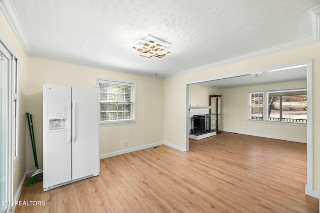 unfurnished living room with a wealth of natural light, light wood-style flooring, ornamental molding, and a fireplace with raised hearth