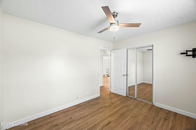 unfurnished bedroom with baseboards, a closet, wood finished floors, and ceiling fan