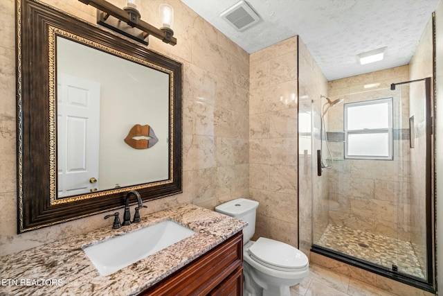 bathroom with tile walls, a textured ceiling, visible vents, a shower stall, and toilet