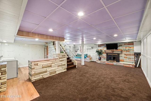 finished basement with stairs, a fireplace with raised hearth, washer / clothes dryer, carpet, and a paneled ceiling