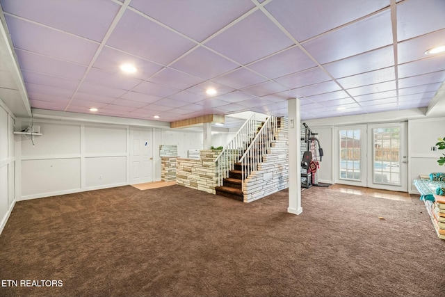 below grade area with a drop ceiling, a decorative wall, carpet floors, and stairs