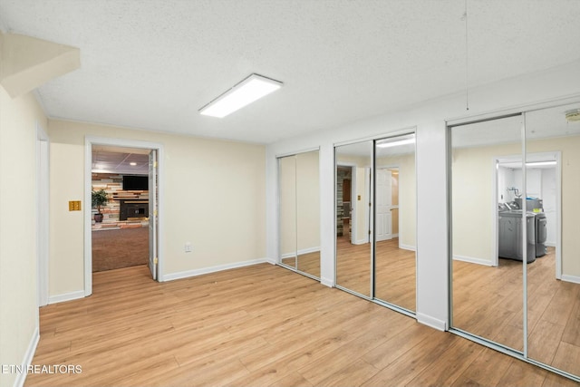unfurnished bedroom featuring multiple closets, washing machine and clothes dryer, wood finished floors, and a textured ceiling
