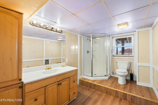 bathroom with a stall shower, toilet, vanity, wood finished floors, and a paneled ceiling