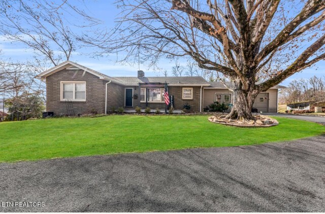 single story home with a chimney, a front yard, an attached garage, and aphalt driveway