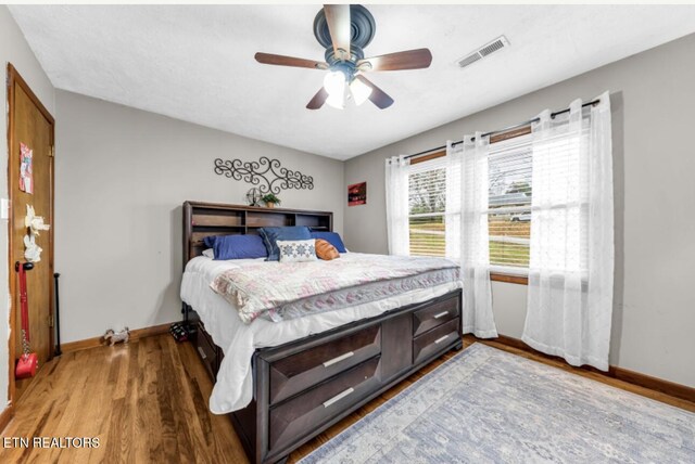 bedroom with a ceiling fan, wood finished floors, baseboards, and visible vents