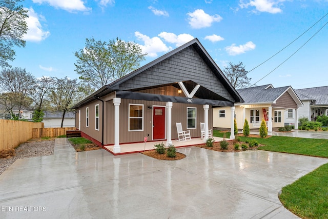 view of front of home with a front yard, board and batten siding, a porch, and fence