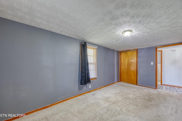 carpeted empty room with baseboards, a textured ceiling, and visible vents