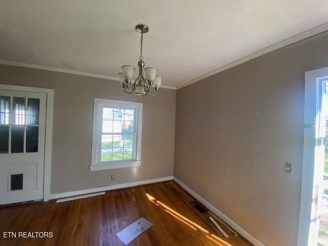 unfurnished dining area with baseboards, ornamental molding, wood finished floors, and a chandelier