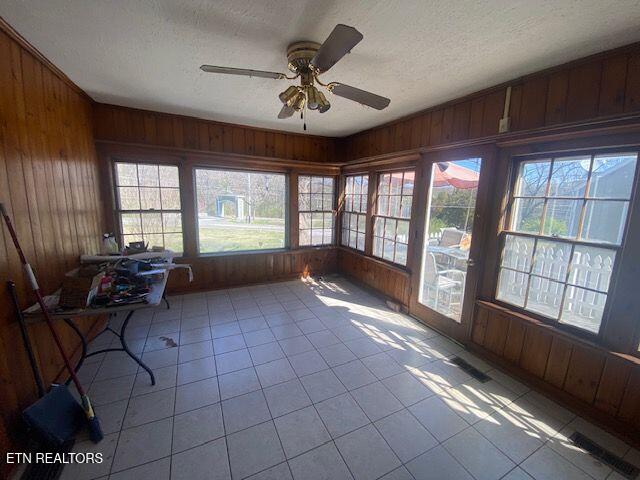 unfurnished sunroom with a textured ceiling, wood walls, and a ceiling fan