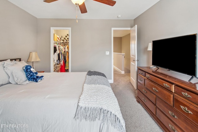 bedroom with a spacious closet, baseboards, a ceiling fan, light carpet, and a closet