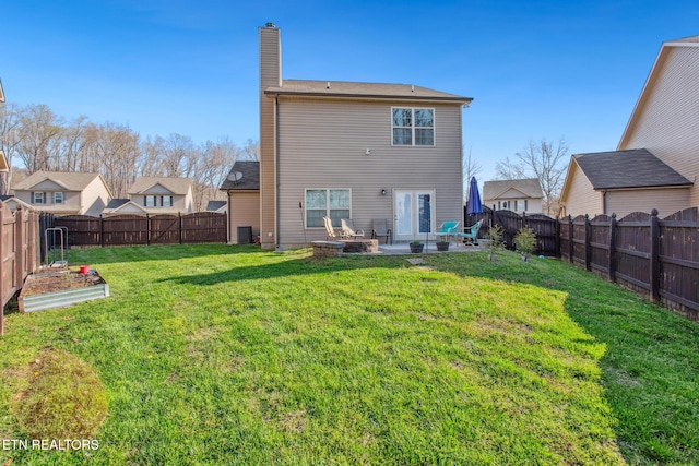 rear view of house featuring a fenced backyard, a chimney, a garden, and a yard