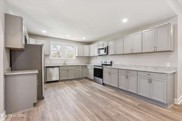 kitchen featuring recessed lighting, light wood-type flooring, gray cabinetry, a sink, and appliances with stainless steel finishes