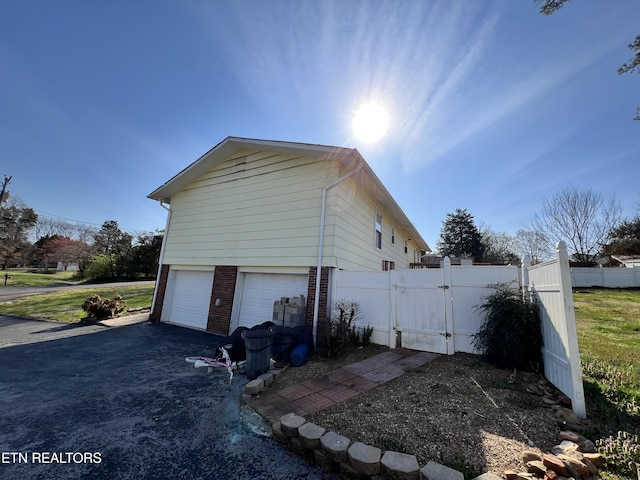 view of home's exterior with a gate, brick siding, a garage, and fence