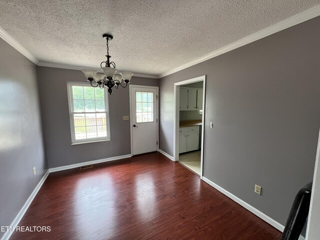 unfurnished dining area with crown molding, an inviting chandelier, a textured ceiling, and dark wood finished floors
