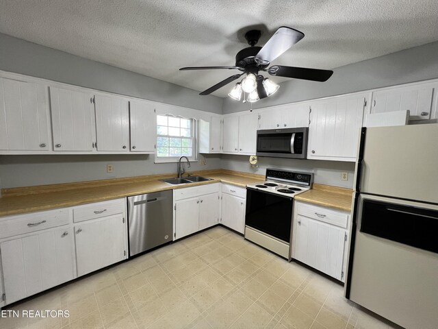 kitchen featuring a ceiling fan, a sink, light floors, white cabinetry, and appliances with stainless steel finishes