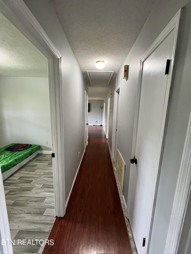 hall with baseboards, wood finished floors, a textured ceiling, and visible vents