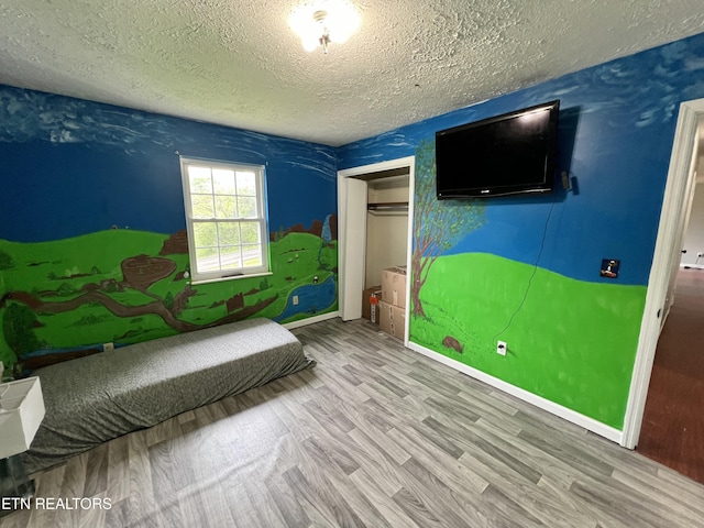 bedroom featuring baseboards, wood finished floors, a textured ceiling, and a closet