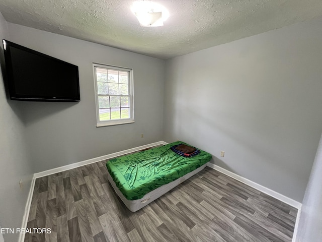 bedroom with wood finished floors, a textured ceiling, and baseboards