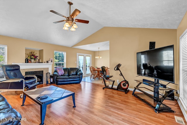 living room featuring light wood-type flooring, a fireplace, visible vents, lofted ceiling, and ceiling fan with notable chandelier