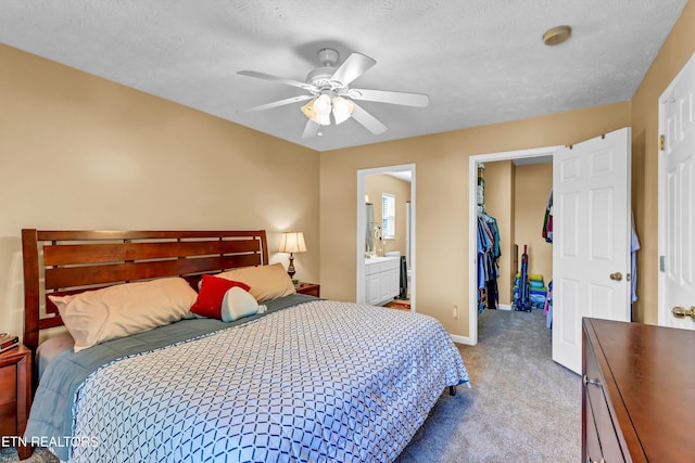carpeted bedroom with a closet, baseboards, ensuite bath, a walk in closet, and ceiling fan