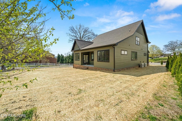 rear view of house with a lawn, a shingled roof, fence, and central AC