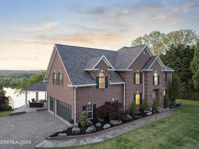 view of property exterior with a garage, a shingled roof, a lawn, decorative driveway, and brick siding