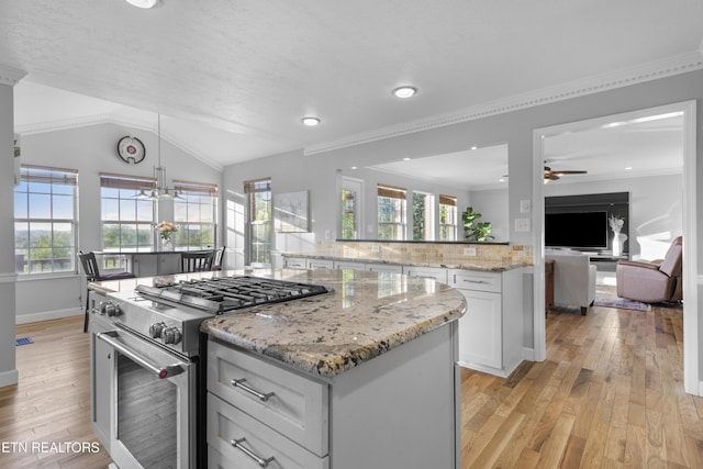 kitchen with decorative backsplash, light wood-type flooring, high end stainless steel range, a kitchen island, and ceiling fan with notable chandelier