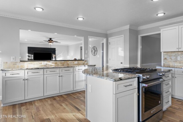 kitchen with tasteful backsplash, light stone counters, stainless steel gas stove, ceiling fan, and light wood-type flooring