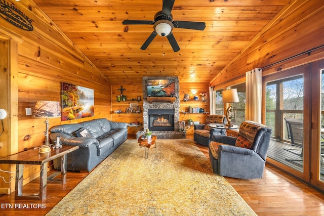 living area with wooden ceiling, wood-type flooring, a stone fireplace, and vaulted ceiling