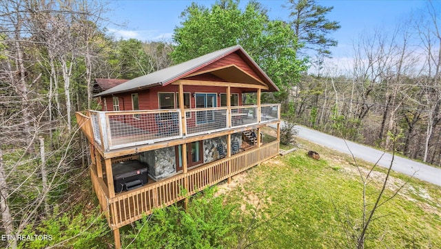 rear view of house featuring a view of trees, stone siding, and a wooden deck