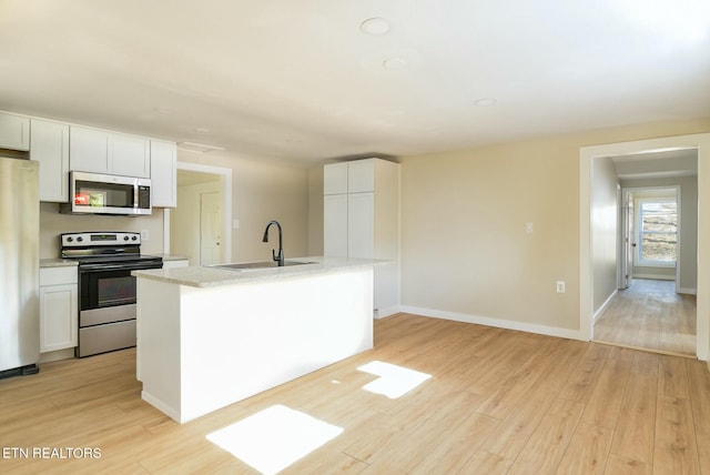 kitchen with a sink, white cabinetry, light wood-style flooring, and appliances with stainless steel finishes