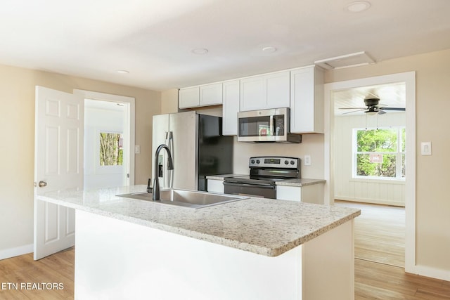 kitchen featuring an island with sink, a sink, light wood finished floors, appliances with stainless steel finishes, and white cabinets