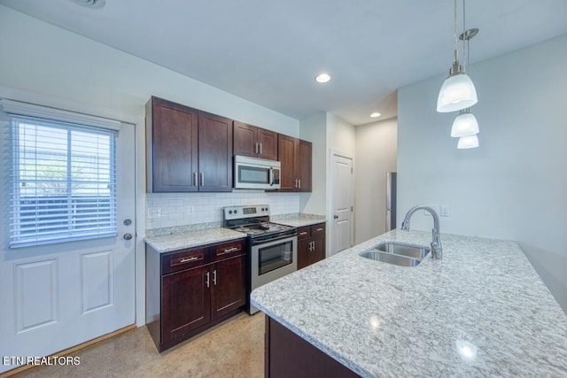 kitchen featuring backsplash, hanging light fixtures, a sink, a peninsula, and appliances with stainless steel finishes