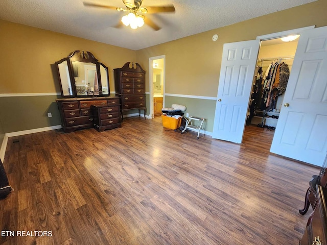 bedroom featuring a textured ceiling, baseboards, ceiling fan, dark wood finished floors, and a spacious closet