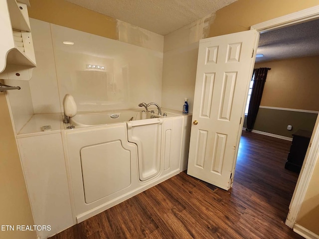 full bath with baseboards, wood finished floors, a bath, and a textured ceiling