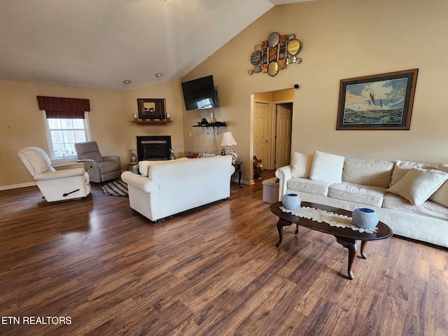 living room featuring dark wood-type flooring, baseboards, high vaulted ceiling, and a glass covered fireplace