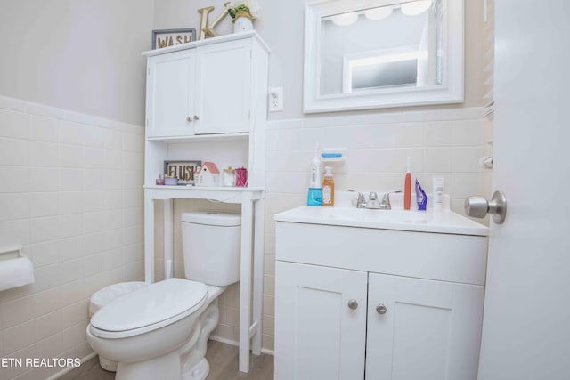 half bathroom featuring wainscoting, toilet, vanity, and tile walls
