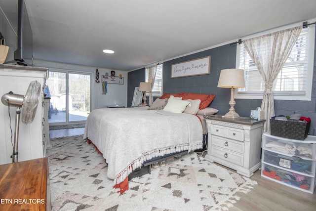 bedroom featuring multiple windows, light wood-style floors, concrete block wall, and access to outside