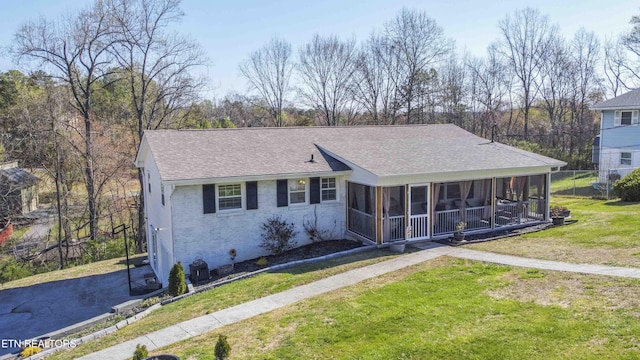 view of front facade featuring brick siding, a sunroom, a front lawn, and a shingled roof