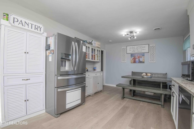 kitchen with light wood-style flooring, stainless steel appliances, light stone counters, visible vents, and white cabinets