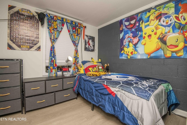 bedroom with concrete block wall, wood finished floors, and ornamental molding