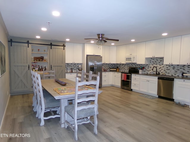 dining room featuring a barn door, a ceiling fan, light wood-style flooring, and recessed lighting