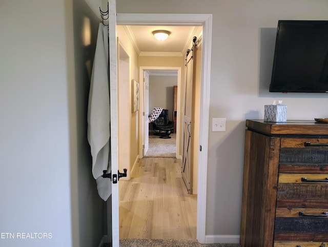 hallway with a barn door, crown molding, light wood finished floors, and baseboards