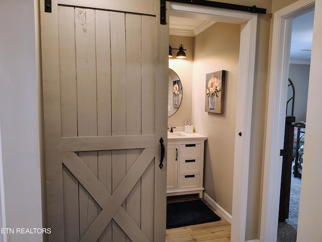 hallway with a sink, a barn door, baseboards, ornamental molding, and wood finished floors