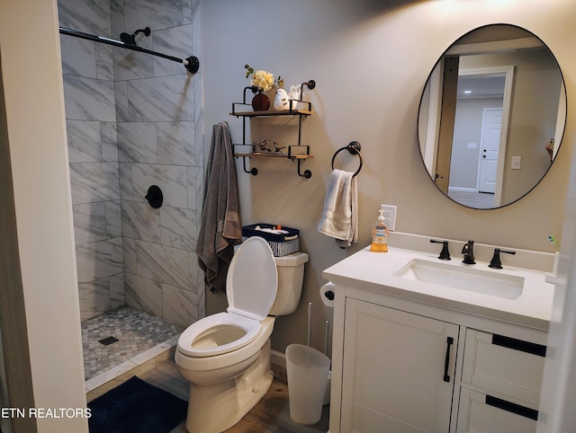 bathroom with toilet, a tile shower, and vanity